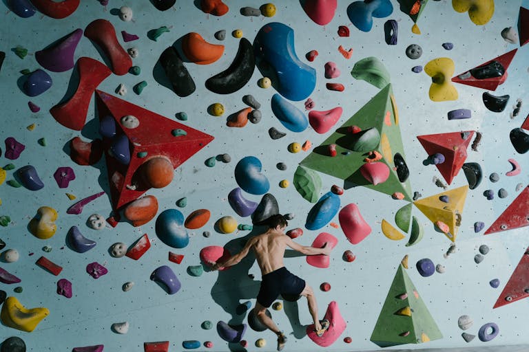 Man bouldering indoors on a colorful climbing wall, showcasing strength and agility.